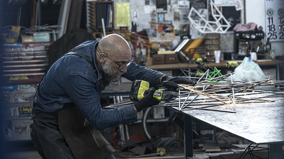 Dion Horstman using angle grinder on metal artwork in workshop