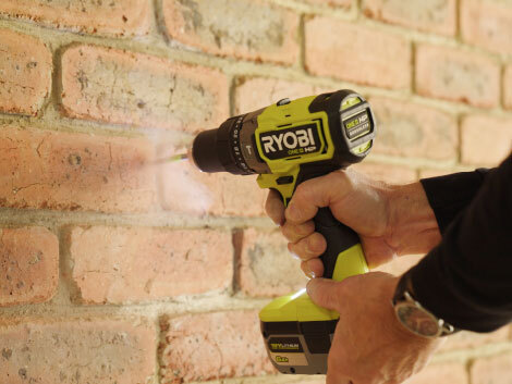 Person drilling into brick wall with RYOBI drill. 