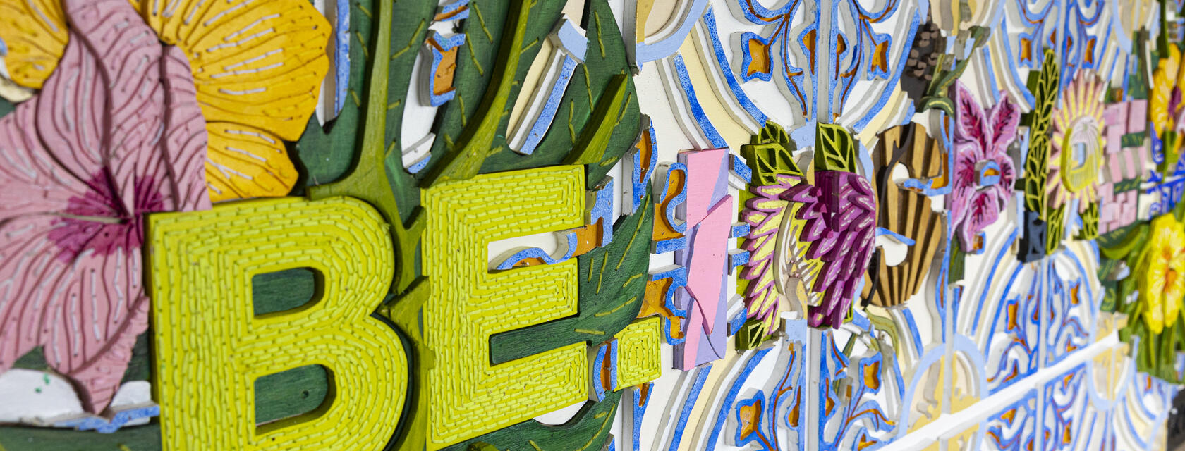 Close up of Be Inspired wooden wall art wording containing bright colours and flower patterns 