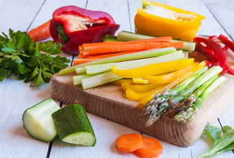 A wooden chopping board with sliced asparagus, capsicum, carrots, zucchini and more