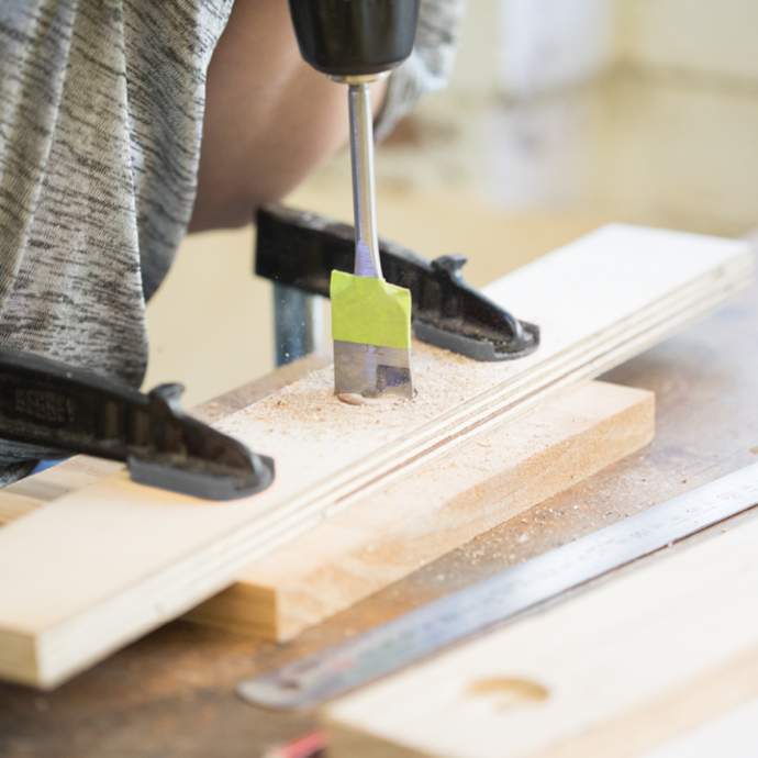 A Ryobi drill driver used to cut a hole in a plank of wood