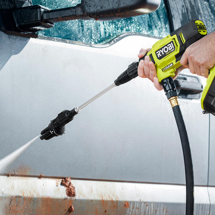 A man uses a Ryobi pressure washer to clean mud off a car